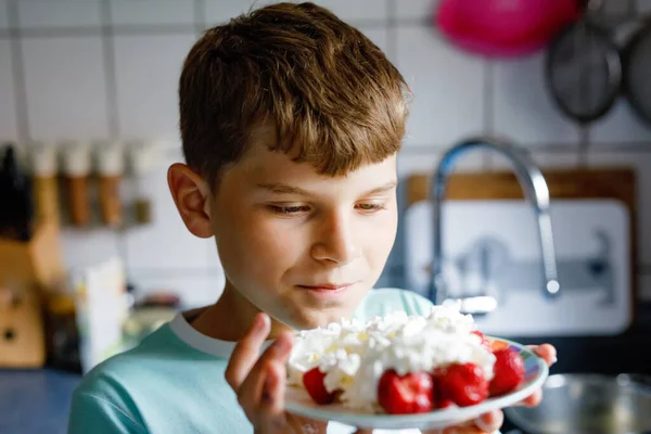 School boy eating fresh strawberries with whipped cream. kid child tasting and biting ripe strawberry. Healthy food, childhood and development. — ストック写真