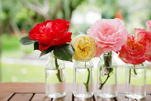 Variante oder Gruppe von Gartenrosen, die in kleinen Vasen oder Flaschen blühen. buntes Blumengesteck oder Dekoration in Regenbogenfarben. Haus oder Garten, Terrassendekoration. — Stockfoto