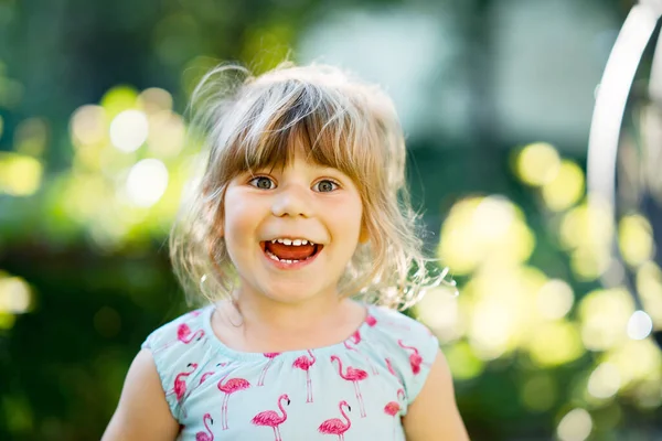 Portret van een vrolijk lachend peutermeisje buiten. Klein kind met blond haar, kijkend en lachend naar de camera. Gelukkig gezond kind genieten van buitenactiviteiten en spelen. — Stockfoto