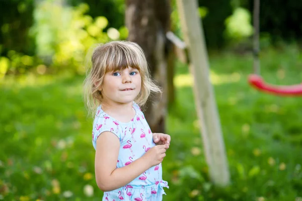 Porträtt av glada leende småbarn flicka utomhus. Ett litet barn med blont hår som tittar och ler mot kameran. Glad frisk barn njuta av utomhus aktivitet och spela. — Stockfoto