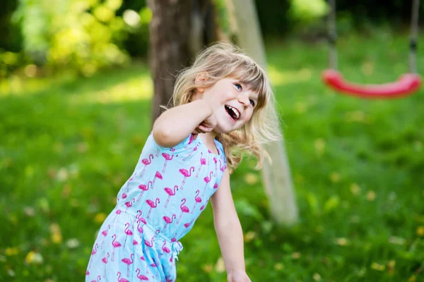 Portret van een vrolijk lachend peutermeisje buiten. Klein kind met blond haar, kijkend en lachend naar de camera. Gelukkig gezond kind genieten van buitenactiviteiten en spelen. — Stockfoto