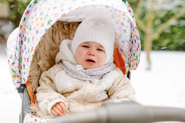 Droevig huilend meisje in de kinderwagen of kinderwagen op winterdag. Ongelukkig overstuur moe en uitgeput kind in warme kleren. Babys eerste sneeuw. Winterwandeling buiten. — Stockfoto