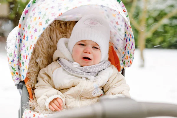 Ragazzina triste che piange seduta nella carrozzina o nel passeggino il giorno d'inverno. Bambino infelice sconvolto stanco ed esausto in vestiti caldi. La prima neve dei bambini. Passeggiata invernale all'aria aperta. — Foto Stock