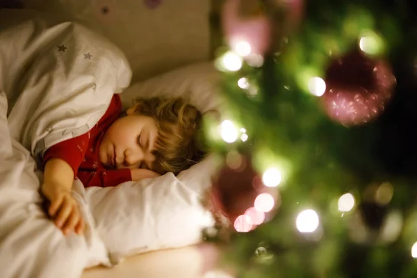 Kleine süße Mädchen schlafen unter dem Weihnachtsbaum und träumen vom Weihnachtsmann zu Hause, drinnen. Traditionelles christliches Fest. Glückliches Kind, das auf Geschenke zu Weihnachten wartet. Kuscheliges weiches Licht — Stockfoto