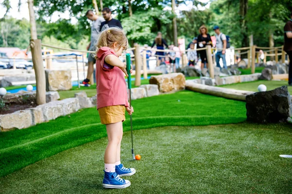 Linda niña preescolar jugando mini golf con la familia. Niño feliz divirtiéndose con la actividad al aire libre. Deportes de verano para niños y adultos, al aire libre. Vacaciones familiares o resort. —  Fotos de Stock