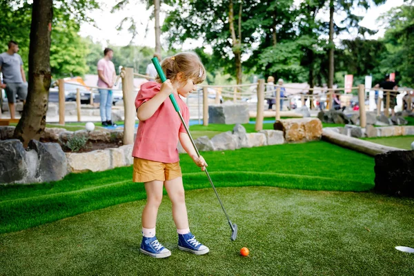 Jolie fille préscolaire jouant au mini golf en famille. Happy enfant en bas âge s'amuser avec l'activité de plein air. Sport d'été pour enfants et adultes, en plein air. Vacances en famille ou station balnéaire. — Photo