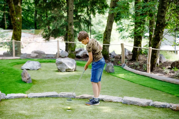Шкільний хлопчик грає в міні-гольф з сім'єю. Щаслива дитина отримує задоволення від активного відпочинку. Літній спорт для дітей та дорослих, на відкритому повітрі. Сімейний відпочинок або курорт . — стокове фото