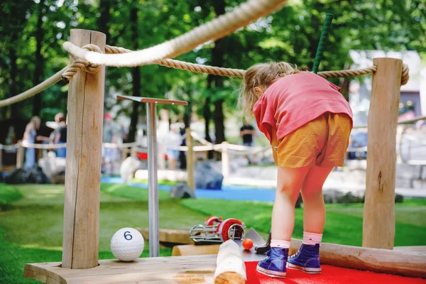 Menina pré-escolar bonito jogar mini golfe com a família. Criança feliz se divertindo com a atividade ao ar livre. Desporto de verão para crianças e adultos, ao ar livre. Férias em família ou resort. — Fotografia de Stock