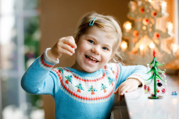 Menina pequena criança sentada à janela e decorando pequena árvore de Natal de vidro com minúsculos brinquedos xmas. A criança sã feliz celebra férias tradicionais de família. Adorável bebê. — Fotografia de Stock