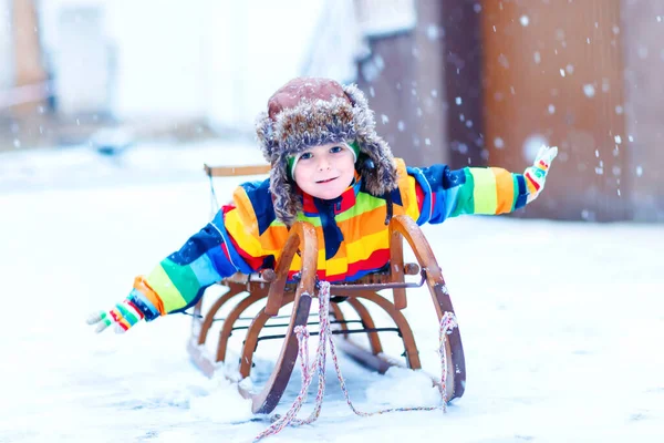 Petit garçon appréciant la randonnée en traîneau pendant les chutes de neige. Joyeux enfant d'âge préscolaire chevauchant sur un traîneau vintage. Les enfants jouent dehors avec la neige. Amusement actif pour les vacances de Noël en famille en hiver — Photo