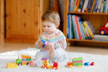Küçük kız evde ya da çocuk odasında eğitici tahta oyuncaklarla oynuyor. Renkli trenle yürüyen çocuk. Çocuk farklı oyuncaklarla eğleniyor. Korona virüsü salgını sırasındaki yalnız çocuk karantina