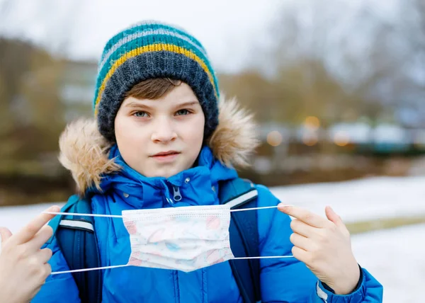 小孩子在上学的路上戴着口罩。儿童背包包。孩子们穿着保暖的衣服，在寒冷的秋天或冬季。日冕大流行病期间的封锁和检疫时间 — 图库照片