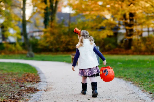 Little toddler girl dressed as a witch trick or treating on Halloween. Happy child outdoors, with orange funny hat and pumpkin bag for sweet haunt. Family festival season in october. Outdoor activity — Stock Photo, Image