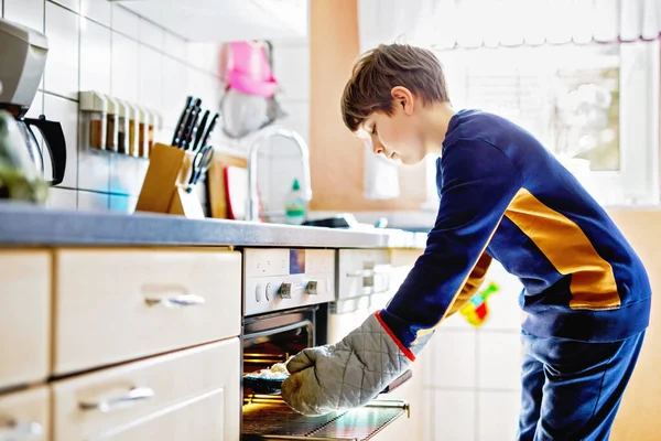 Happy blond écolier garçon cuisson muffins vanille myrtille dans la cuisine domestique, à l'intérieur. drôle belle sain enfant avoir amusant avec aider. — Photo