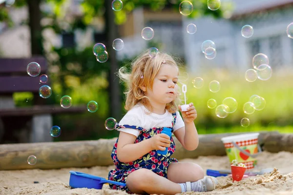 Linda menina criança loira pequena se divertindo com soprando soprador de bolhas de sabão. Bonito bebê adorável criança brincando no playground no dia ensolarado de verão. Criança saudável engraçado ativo feliz — Fotografia de Stock