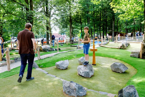 Un écolier jouant au mini golf avec son père. Joyeux enfant et papa, jeune homme qui s'amuse avec l'activité de plein air. Sport d'été pour enfants et adultes, en plein air. Vacances en famille ou station balnéaire. — Photo