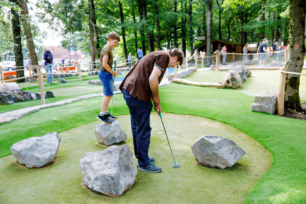 школьник играет с отцом в мини-гольф. счастливый ребенок и папа, молодой человек, весело проводящий время на свежем воздухе. Летний спорт для детей и взрослых, на открытом воздухе. семейный отдых или курорт.