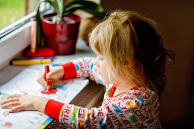 Salgın koronavirüs hastalığı sırasında boya kalemleriyle resim yapan küçük bir kız. Çocuklar resim yapar ve çizer, yaratıcı sanat ve eğitim kavramı. Mutlu çocuk