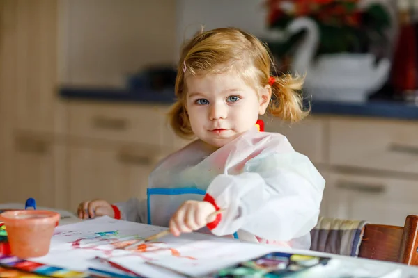 귀엽고 귀여운 여자 애가 물감으로 그림을 배우고 있어. 어린아이들은 화려 한 붓을 사용하여 집에서 그림을 그리고 있다. 건강 한 딸 이 색깔, 집에서 물을 가지고 실험을 하거나 보육원에서 물을 마시는 모습 — 스톡 사진