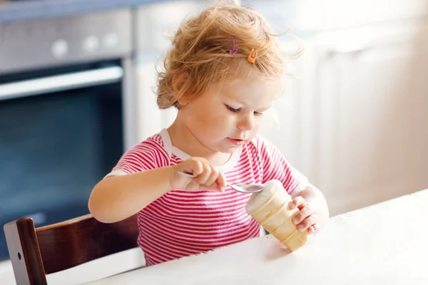 Menina adorável comendo de colher sorvete doce em cone de waffle. conceito de alimentação, criança, alimentação e desenvolvimento. Criança bonito, filha com colher sentada em cadeira alta e aprendendo a comer por si só — Fotografia de Stock