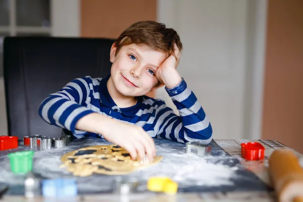 Lustig fröhlicher gesunder Schuljunge, der zu Hause Lebkuchen backt. Liebenswertes blondes kleines Kind, das in der heimischen Küche seinen Spaß hat. Traditionelle Freizeit mit Kindern an Weihnachten. — Stockfoto