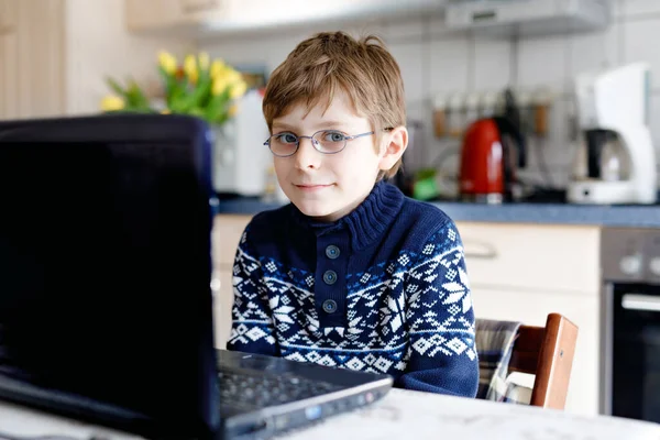 Мальчик в очках учится дома на ноутбуке для школы. Очаровательный ребенок делает домашнее задание и с помощью ноутбука и современных гаджетов. Концепция домашнего обучения. — стоковое фото