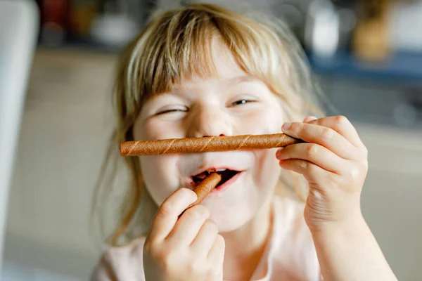 Çikolatalı gözleme tutan mutlu küçük anaokulu kızının portresi. Tatlı bisküvi ekmeğiyle gülümseyen aç bir çocuk. Tatlı kakaolu waffle. — Stok fotoğraf