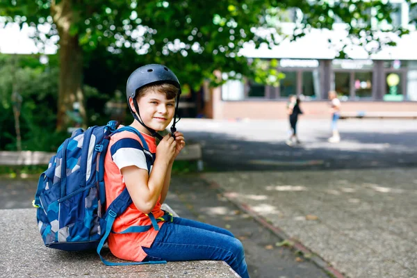 Niño feliz con mochila y casco de bicicleta. Colegial en el camino a la escuela media o secundaria. Niño sano y adorable al aire libre en el patio de la escuela. De vuelta a la escuela. Construyendo sobre el fondo. — Foto de Stock