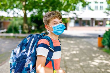Okula giderken maske takan çocuk. Sırt çantalı çocuk. Yaz tatilinden sonra okula dönüyorum. Korona salgını sırasında korunma. Okul bahçesinde binası olan sağlıklı bir çocuk.