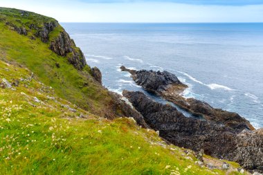 Malin Head, Donegal, İrlanda 'da engebeli bir manzara. Kayalıkları olan dalgalı bir sahil, sisli bulutlu bir günde koyunlu yeşil kayalık bir arazi..