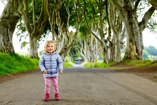 Nettes Kleinkind Mädchen zu Fuß an einem regnerischen Tag zu Beginn von The Dark Hedges. Nordirland. Glückliches Kind zu Besuch bei Eltern und Familie berühmte irische Baumallee — Stockfoto