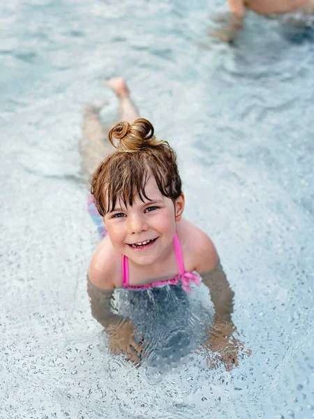 Ένα μικρό κορίτσι προσχολικής ηλικίας που πιτσιλάει σε μια εξωτερική πισίνα τη ζεστή καλοκαιρινή μέρα. Ευτυχισμένο υγιές παιδί μικρό παιδί απολαμβάνει ηλιόλουστο καιρό στη δημόσια πισίνα της πόλης. Παιδική δραστηριότητα σε εξωτερικούς χώρους με νερό. — Φωτογραφία Αρχείου