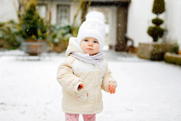 Ragazzina felice fare i primi passi all'aperto in inverno attraverso la neve. Bel bambino che impara a camminare. Bambino che si diverte nella fredda giornata innevata. I bambini prima neve, attività. Passeggiata invernale all'aria aperta — Foto Stock