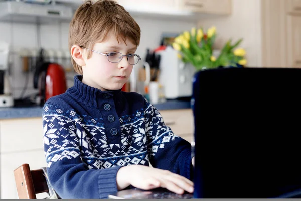 Junge mit Brille lernt zu Hause am Laptop für die Schule. Entzückendes Kind, das Hausaufgaben macht und Notizbuch und moderne Geräte benutzt. Heimschulkonzept. — Stockfoto