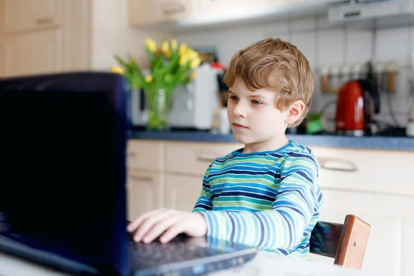 Мальчик учится дома на ноутбуке для школы. Элементарный школьник делает домашнюю работу, используя ноутбук и современные гаджеты. Концепция домашнего обучения. Видеоуроки с учителем. — стоковое фото