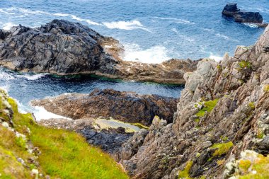 Malin Head, Donegal, İrlanda 'da engebeli bir manzara. Kayalıkları olan dalgalı bir sahil, sisli bulutlu bir günde koyunlu yeşil kayalık bir arazi..