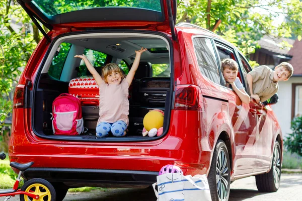 Tři děti, dva chlapci a školačka sedící v autě před odjezdem na letní prázdniny s rodiči. Šťastné děti, sourozenci, bratři a sestry s kufry a hračkami na rodinný výlet — Stock fotografie