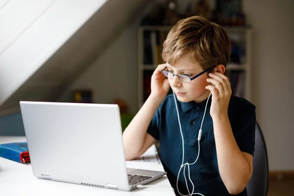 Kid boy with glasses learning at home on laptop for school. Adorable child making homework and using notebook and modern gadgets. Home schooling concept. — Stock Photo, Image