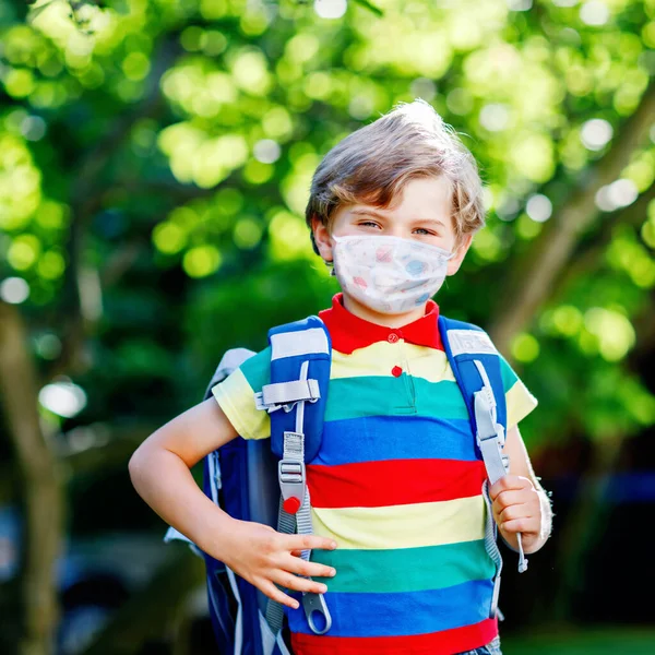 Rapazinho feliz, máscara médica, mochila ou mochila. Um estudante a caminho da escola. Criança saudável ao ar livre. De volta à escola após o tempo de quarentena do bloqueio da doença pandêmica da corona — Fotografia de Stock