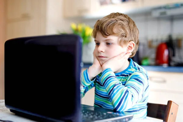 Grabben lär sig hemma på laptop för skolan. Grundskolebarn som gör läxor och använder anteckningsblock och moderna prylar. Hemskolekoncept. Att ha en videolektion med lärare. — Stockfoto