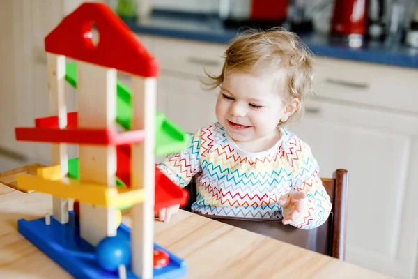 Bambina che gioca con i giocattoli educativi a casa o nella scuola materna. Felice bambino bambino sano che si diverte con la pista di palla giocattolo in legno colorato. Il ragazzo impara a tenere e rotolare le palle. Educazione motoria. — Foto Stock