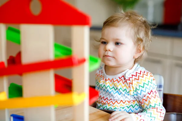 Kleine Mädchen spielen zu Hause oder im Kinderzimmer mit Lernspielzeug. Fröhliches gesundes Kleinkind, das Spaß an der bunten Kugelbahn aus Holz hat. Kind lernt Bälle zu halten und zu rollen. Motorische Bildung. — Stockfoto