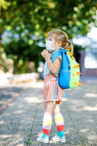 놀이방가는 첫날, 코로나 코비 드 바이러스에 대항하는 의료용 마스크를 쓰고 걸음마하는 여자아이. 보육원이나 유치원으로 걸어가는 건강하고 아름다운 아기. 가방을 든 행복 한 아이 — 스톡 사진