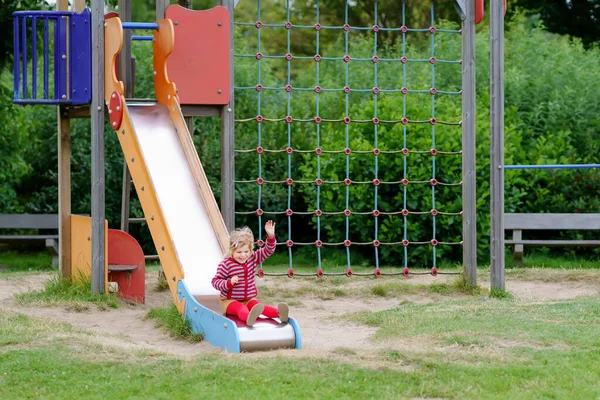 Petite fille d'âge préscolaire jouant sur une aire de jeux extérieure. Happy enfant en bas âge escalade et s'amuser avec l'activité de plein air de l'été. fille slinding vers le bas l 'diapositive. — Photo