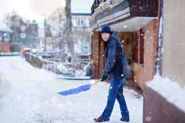 Man med snöskyffel rengör trottoarer på vintern under snöfall. Vintertid i Europa. Unge man i varma vinterkläder. Snö- och väderkaos i Tyskland. Snöstorm och tung snö. Schneechaos — Stockfoto