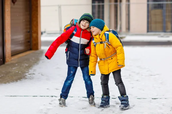 下大雪时，两个小学的小男孩步行去学校。快乐的孩子们玩的开心，玩的是初雪。穿着五颜六色冬衣背着背包的兄弟姐妹和好朋友. — 图库照片