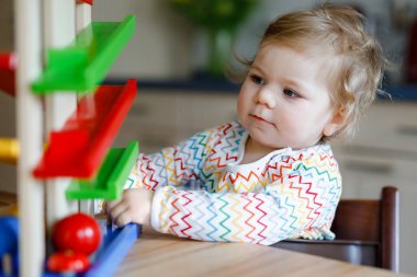 Küçük kız evde ya da çocuk odasında eğitici oyuncaklarla oynuyor. Mutlu sağlıklı çocuk renkli tahta top pisti ile eğleniyor. Çocuk top tutmayı ve yuvarlanmayı öğreniyor. Motorik eğitim.