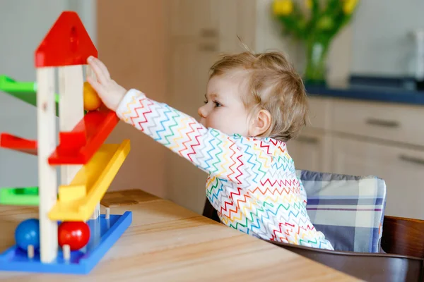 Pequena menina brincando com brinquedos educativos em casa ou berçário. Criança infantil saudável feliz se divertindo com pista de bola de brinquedo de madeira colorida. Criança aprendendo a segurar e rolar bolas. Ensino motorizado. — Fotografia de Stock