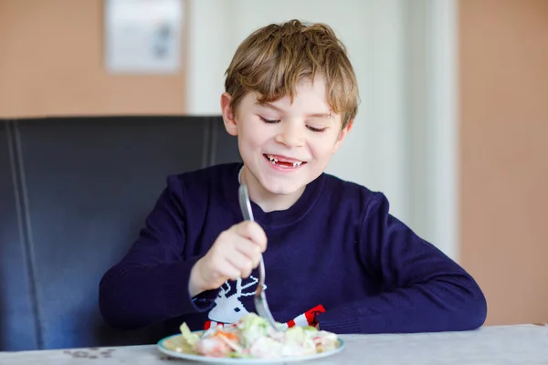 Happy kid boy eating fresh salad with tomato, cucumber and different vegetables as meal or snack. Healthy child enjoying tasty and fresh food at home or at school canteen. — Stock Photo, Image