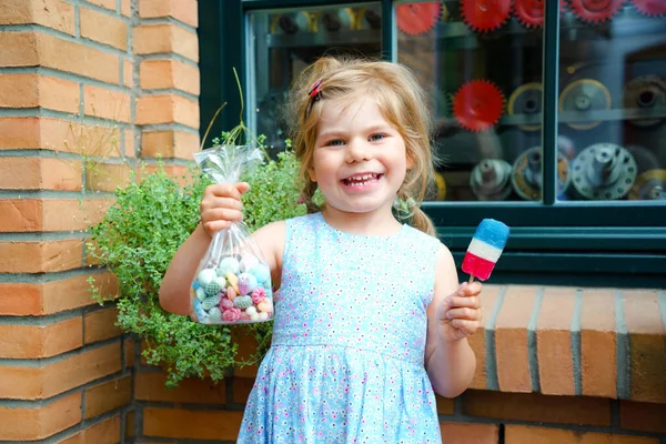 Pequena menina pré-escolar com saco com bombons e pirulito. Bonito criança feliz lambendo doce açúcar lolli. Criança feliz com doces. — Fotografia de Stock